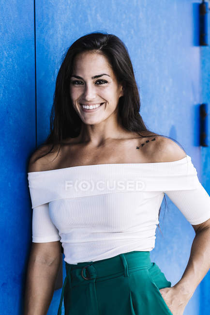 Портрет упевненої усмішки молодої жінки до синьої стіни. — стокове фото