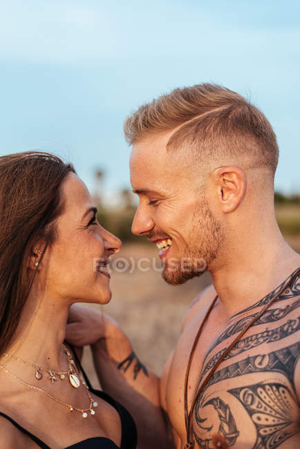 Senza maglietta tatuato maschio e sensuale donna in costume da bagno in piedi vicino e guardando lontano con cielo blu sullo sfondo in Spagna — Foto stock