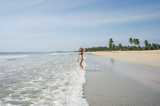Jovem mulher na água na praia de areia com floresta tropical — Fotografia de Stock