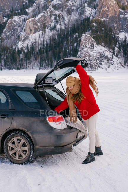 Female traveler standing in snowy valley and opening car trunk — Stock Photo