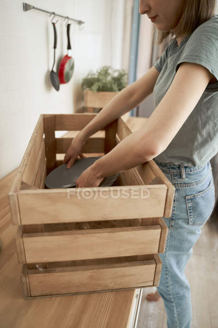 Frau in Freizeitkleidung packt Geschirr in Holzkiste an Theke in Küche — Stockfoto