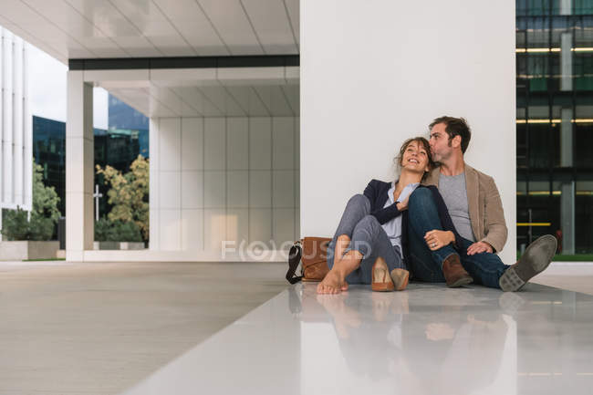 Чоловік менеджер обіймає і цілує дівчину, сидячи за межами офісної будівлі на міській вулиці після роботи — стокове фото