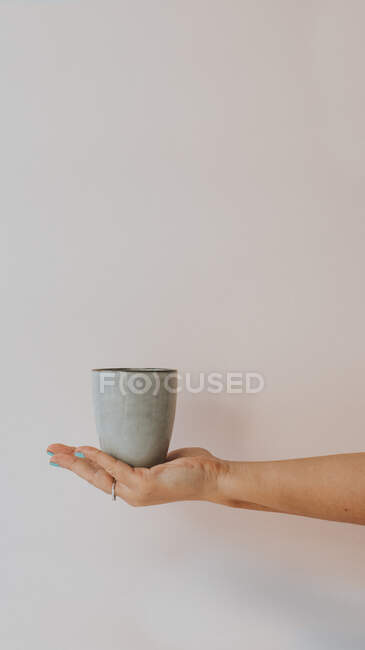Large gray mug with drink in hand of crop person on white background — Stock Photo