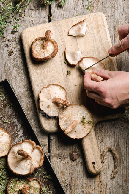 Зверху готують ріжучі шапки зі свіжих коричневих грибів шиітаке на дерев'яній обробній дошці за сільським столом — стокове фото
