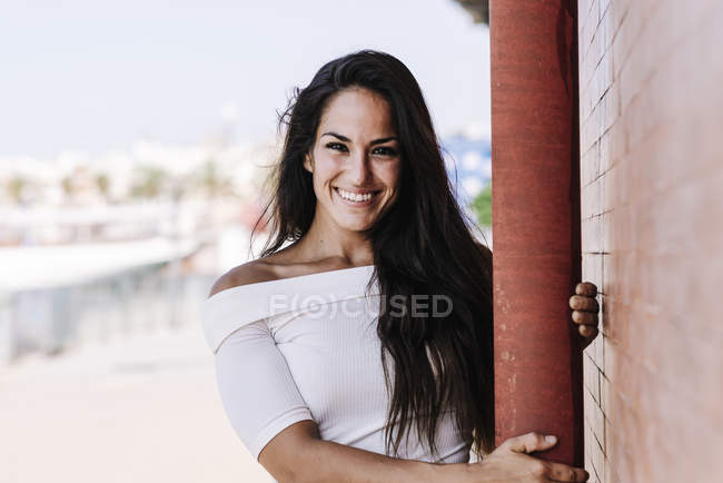 Beautiful smiling young woman hanging on a pole in the street while looking camera — Stock Photo
