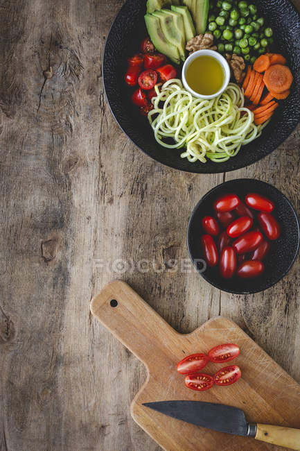 Цуккини сырой веганской пасты с горохом, помидоры черри, авокадо, морковь, орехи и оливковое масло в миске служил на деревянном фоне — стоковое фото