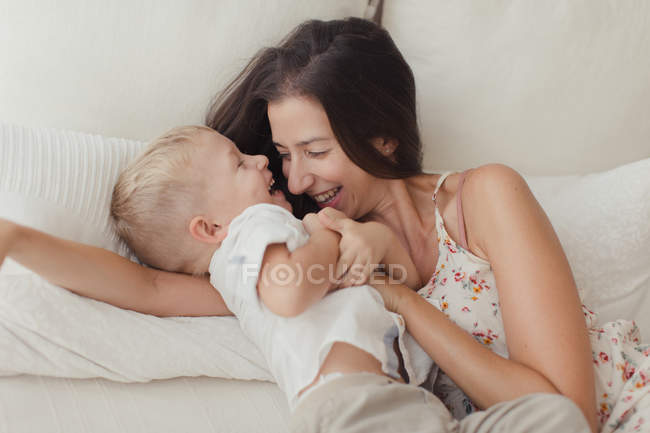Morena satisfecha abrazando feliz hijo pequeño en la cama - foto de stock