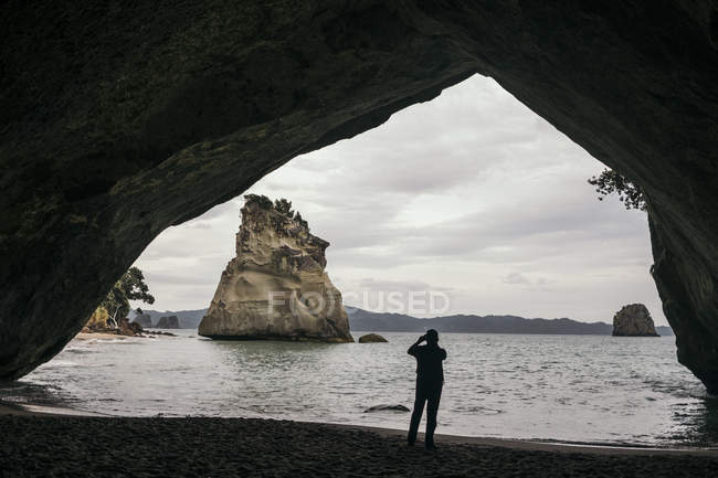 Voltar vista de turista de pé e tirando foto de praia exótica com grandes rochas na caverna na praia Cathedral cove na Nova Zelândia — Fotografia de Stock