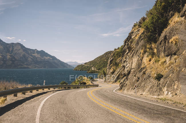 Asphalt road and tropical green cliffs and blue lake with cloudy blue sky and Mountain Cook in New Zealand — Stock Photo
