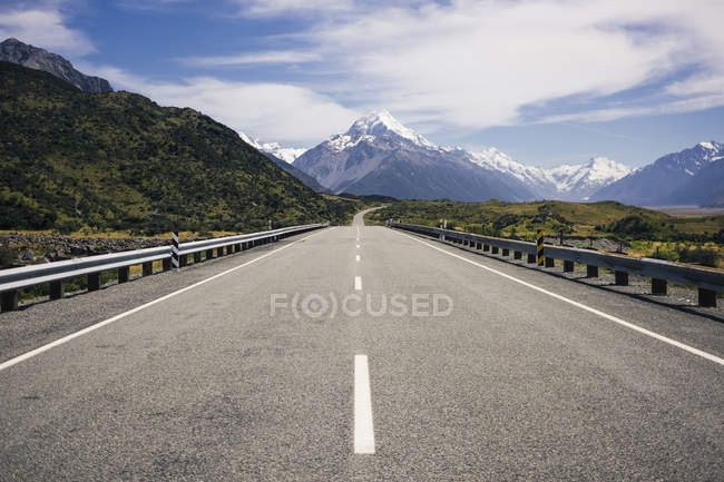 Asphalt road and tropical green cliffs and blue lake with cloudy blue sky and Mountain Cook in New Zealand — Stock Photo