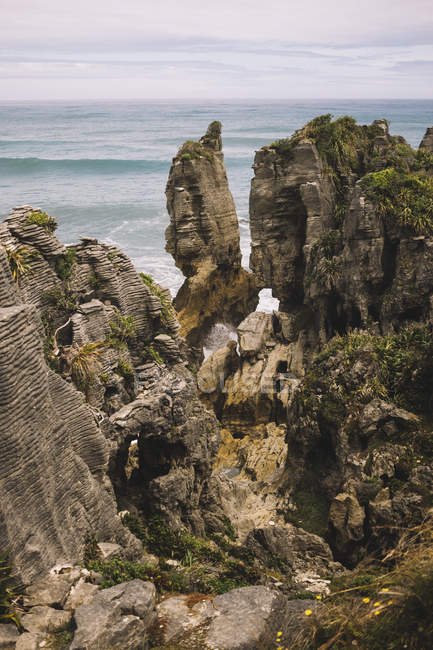 De cima de rochoso coberto de plantas litoral com ondas e céu nublado em Pancake Rocks na Nova Zelândia — Fotografia de Stock