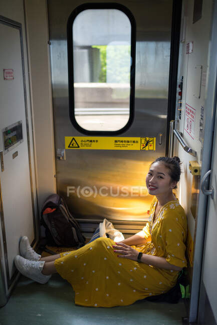 Von oben sieht man asiatische Urlauberin im trendigen gelben Kleid im Zug sitzen, während sie in Schottland lächelt und in die Kamera blickt — Stockfoto