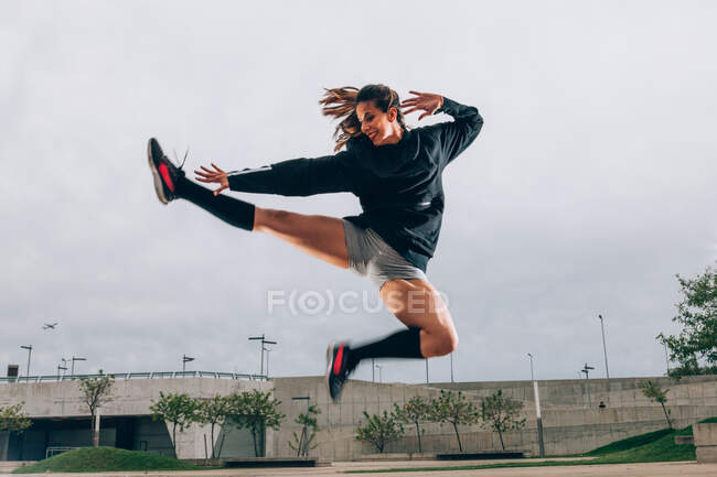 Dançarina feminina no desgaste ativo sorrindo enquanto dança no salto ao ar livre — Fotografia de Stock