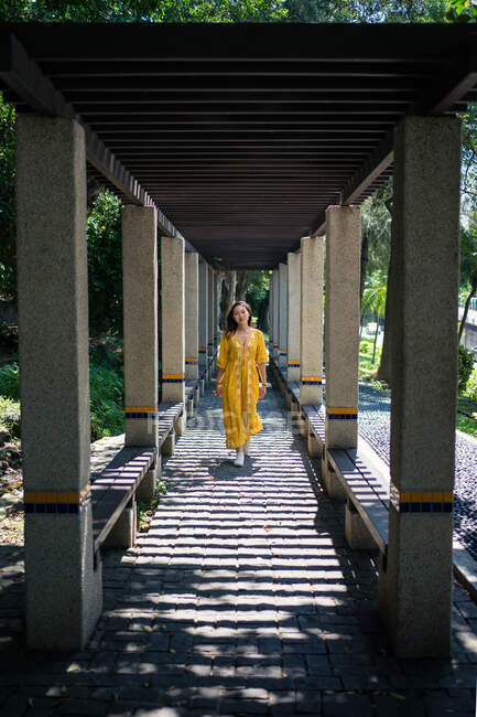 Молодая туристка в стильном желтом платье гуляет среди качающейся аллеи с зелеными растениями и смотрит в камеру в Шотландии — стоковое фото