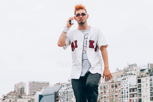 Adolescente masculino contemporáneo en ropa casual de moda llamando en el teléfono inteligente - foto de stock