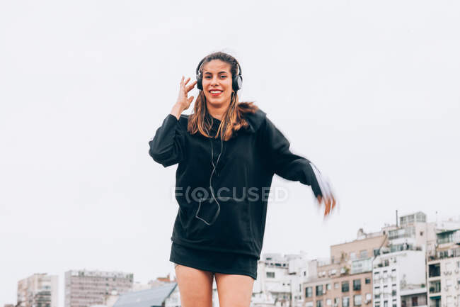 Contenuto giovane donna in abbigliamento casual danza durante l'utilizzo di cuffie in strada città — Foto stock