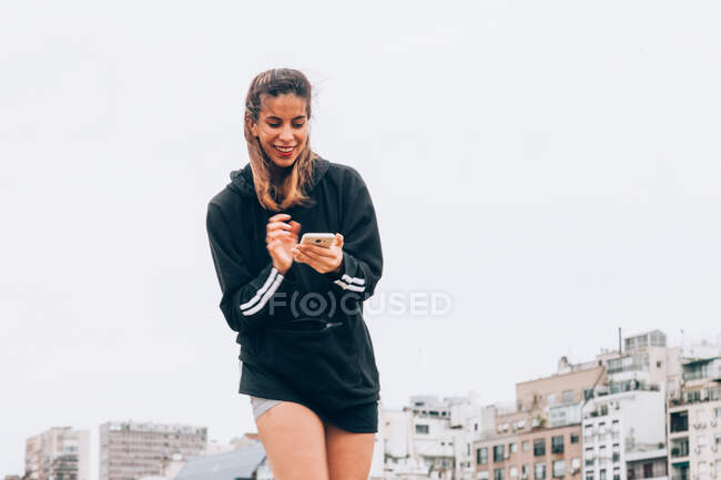 Zufriedene junge Frau in Freizeitkleidung surft auf Smartphone in der City Street — Stockfoto