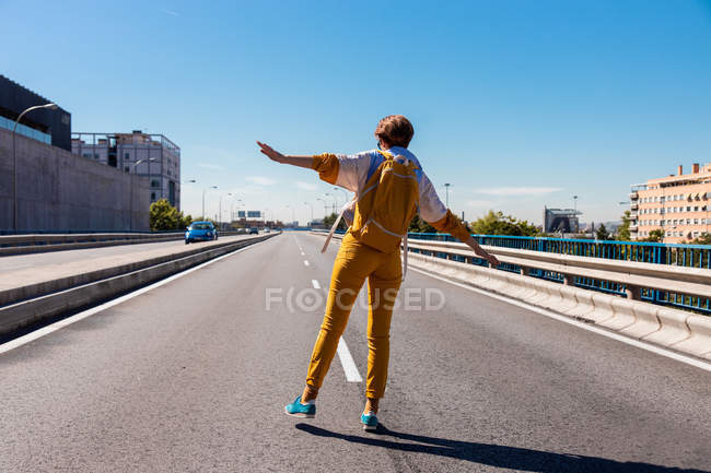 Back view of courageous girl in trendy yellow clothes and blue shoes with backpack balancing on city street — Stock Photo