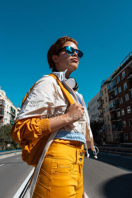 Яскрава тисячолітня жінка в стильних сонцезахисних окулярах насолоджується видом на вулицю міста. — стокове фото