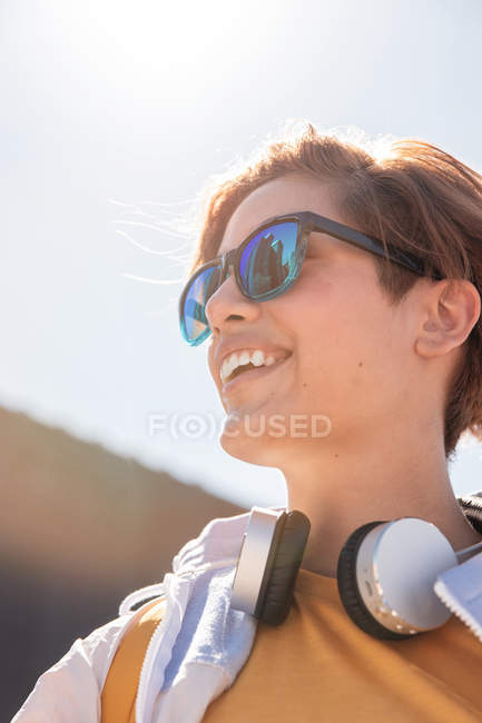 Low angle bright millennial in stylish sunglasses enjoying view while looking away against blurred city street — Stock Photo