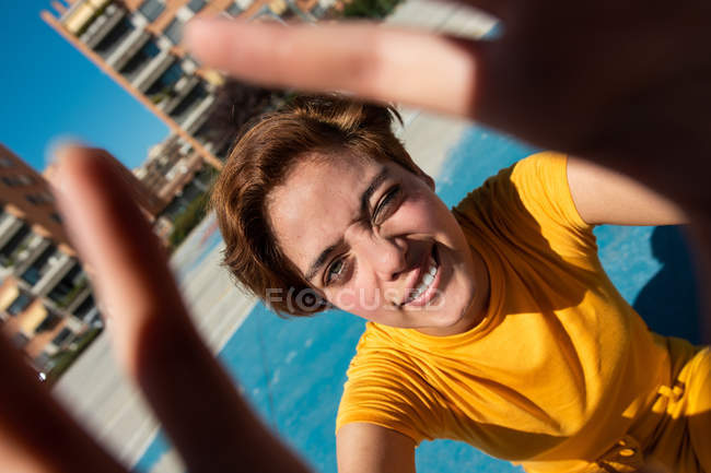 Cooler Teenager in gelben Klamotten blickt in die Kamera und zeigt Hände auf blauem Sportplatz — Stockfoto