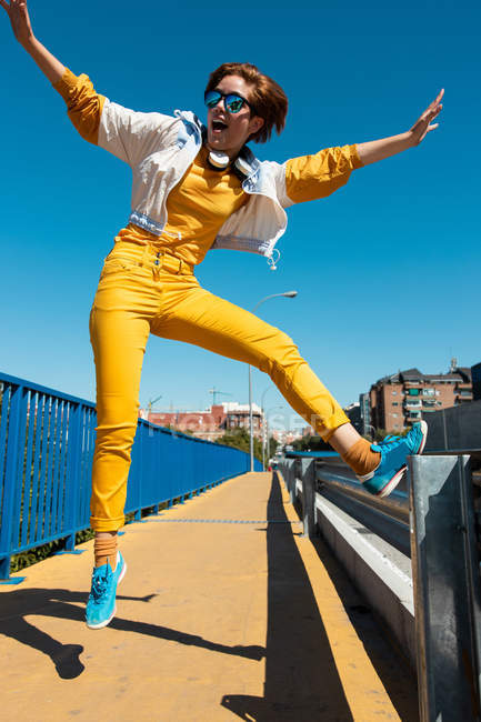 From below cheerful courageous teenager in sunglasses jumping with mouth open and arms raised on street — Stock Photo