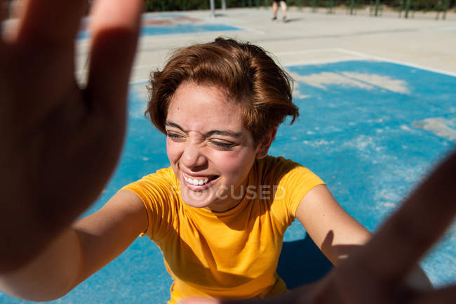 Hoher Winkel cooler Teenager in gelben Klamotten mit geschlossenen Augen, der Hände auf blauem Sportplatz zeigt — Stockfoto