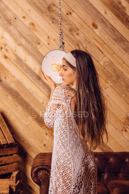 Young woman posing between ceiling lamps on wooden background — Stock Photo