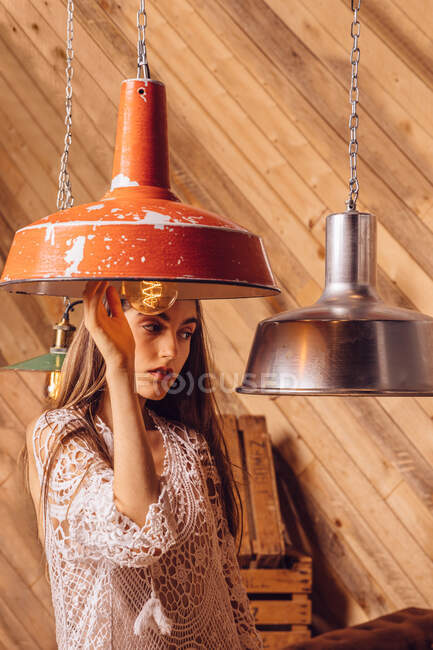 Young woman posing between ceiling lamps on wooden background — Stock Photo