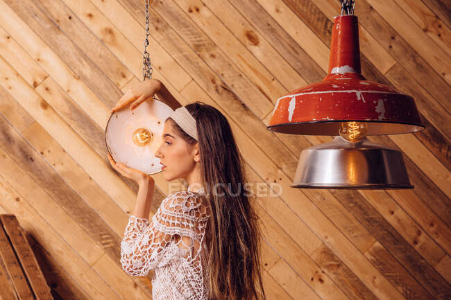 Giovane donna in posa tra le lampade a soffitto su sfondo di legno — Foto stock