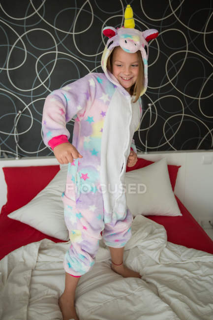 Fröhliches Mädchen im Einhorn-Pyjama hat Spaß auf dem Bett — Stockfoto