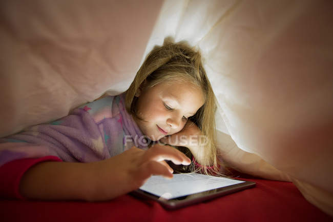 Positives Vorschulmädchen mit Tablette unter Decke im Bett — Stockfoto