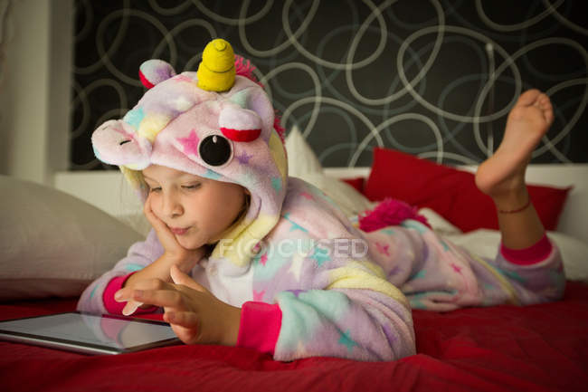 Girl in unicorn pajama using tablet on bed — Stock Photo