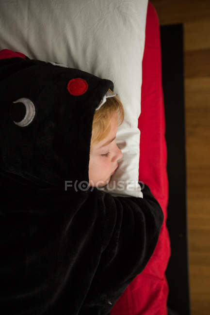 Мальчик в черном пижаме кигуруми спит в постели. — стоковое фото
