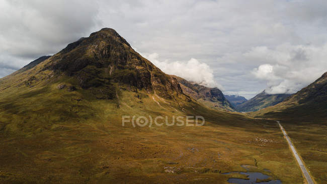 Desde arriba hermoso paisaje de camino vacío a través del prado verde y marrón en el valle a lo largo del río sinuoso en Escocia - foto de stock