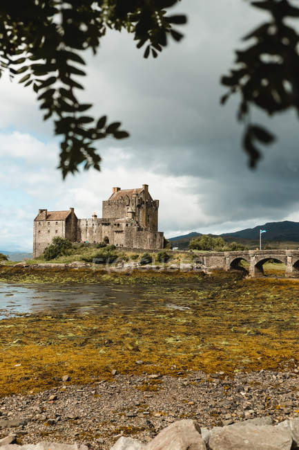 Amazing scenery of abandoned medieval castle with cobblestone bridge across swampy shore under dramatic sky in Scotland — Stock Photo