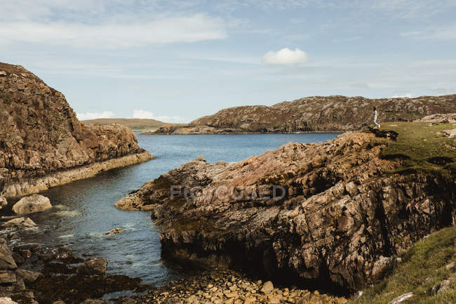 Hermoso paisaje escénico de la bahía rocosa con persona solitaria de pie sobre acantilados en Escocia - foto de stock