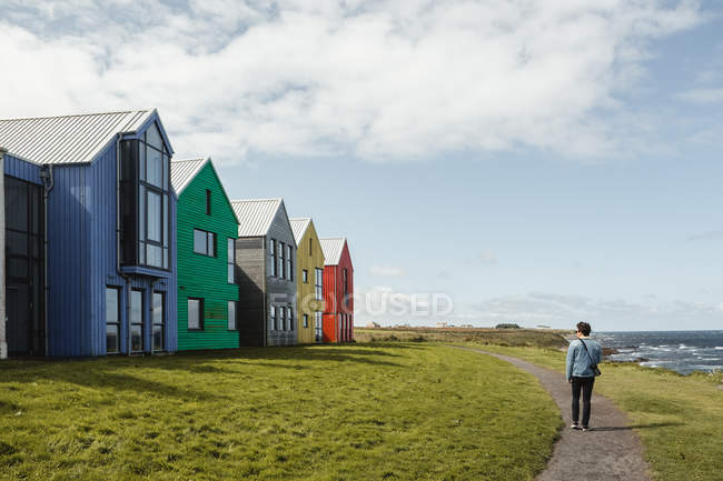 Vista posteriore del viaggiatore maschio che cammina sul sentiero nel villaggio con case colorate e paesaggio panoramico al mare scozzese — Foto stock