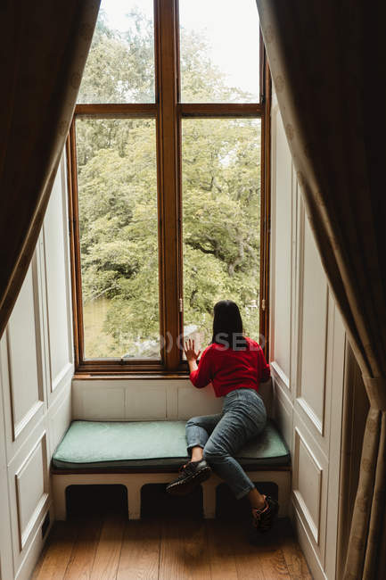 Visão traseira do viajante feminino sentado no banco e olhando através da janela enquanto visita a casa velha na Escócia — Fotografia de Stock