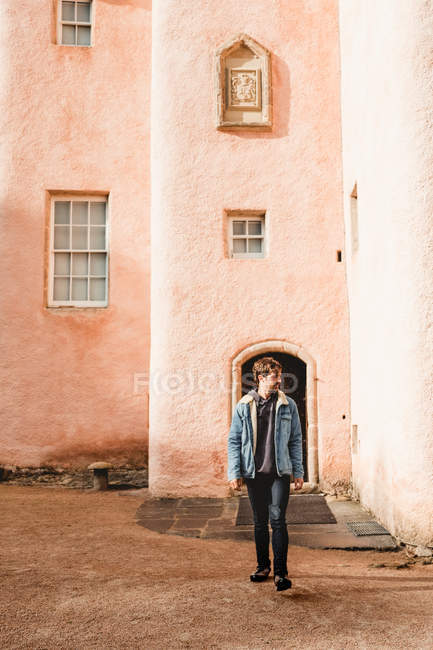 Молодой путешественник, стоящий во дворике средневекового каменного замка с розовыми стенами во время тура по Шотландии — стоковое фото