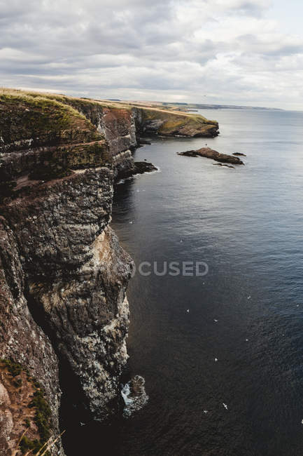 Costa rocciosa tra tranquille acque oceaniche durante il giorno soleggiato in Scozia — Foto stock