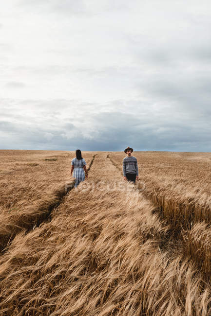 Женщина в платье и мужчина в шляпе идут в противоположных направлениях по параллельным тропинкам среди безграничного шотландского поля — стоковое фото