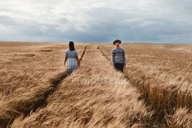 Woman in dress and man in hat walking in opposite directions on parallel footpaths among boundless Scottish field — Stock Photo