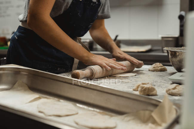 Side view midsection of baker in black apron rolling dough on table with white flour while making flat bread in kitchen — Stock Photo