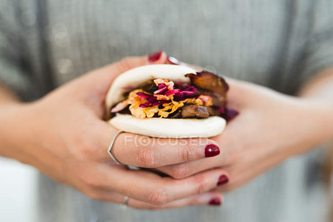 Du haut des mains de la femme tenant un sandwich au pain à la vapeur asiatique traditionnel avec de la viande et des légumes — Photo de stock