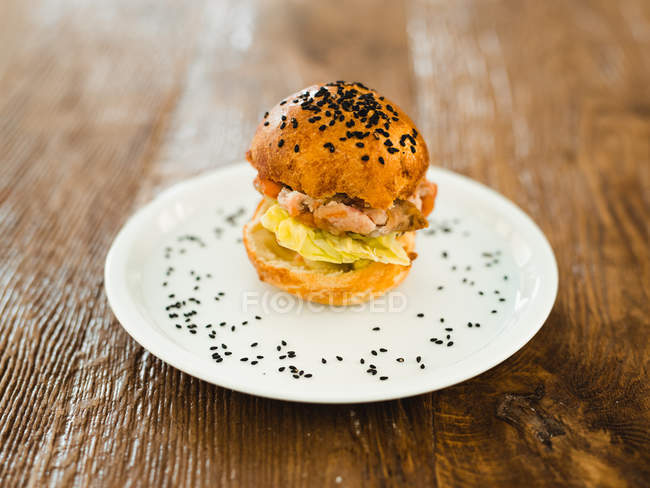 Hamburger appétissant avec petit pain croustillant et sésame noir posé sur une table en bois — Photo de stock