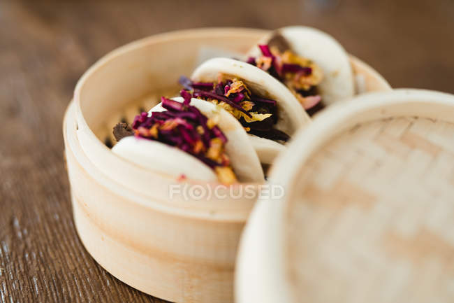 Close-up of traditional Asian steamed bun sandwiches with meat and vegetables in bamboo steamer placed in wooden table — Stock Photo