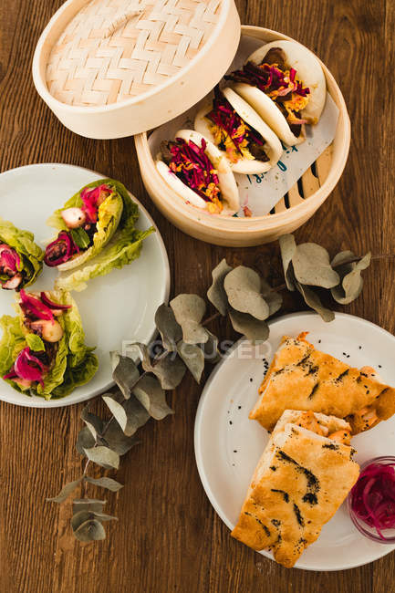 Various selection of different Asian dishes on plates placed in wooden table — Stock Photo