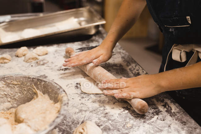 Vista lateral do padeiro mãos rolando massa na mesa com farinha branca ao fazer pão liso na cozinha — Fotografia de Stock