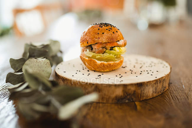 Апетитний смачний гамбургер з хрусткою булочкою, подається в круглому дерев'яному лотку, розміщеному на дерев'яному столі поруч з гілкою рослини — стокове фото